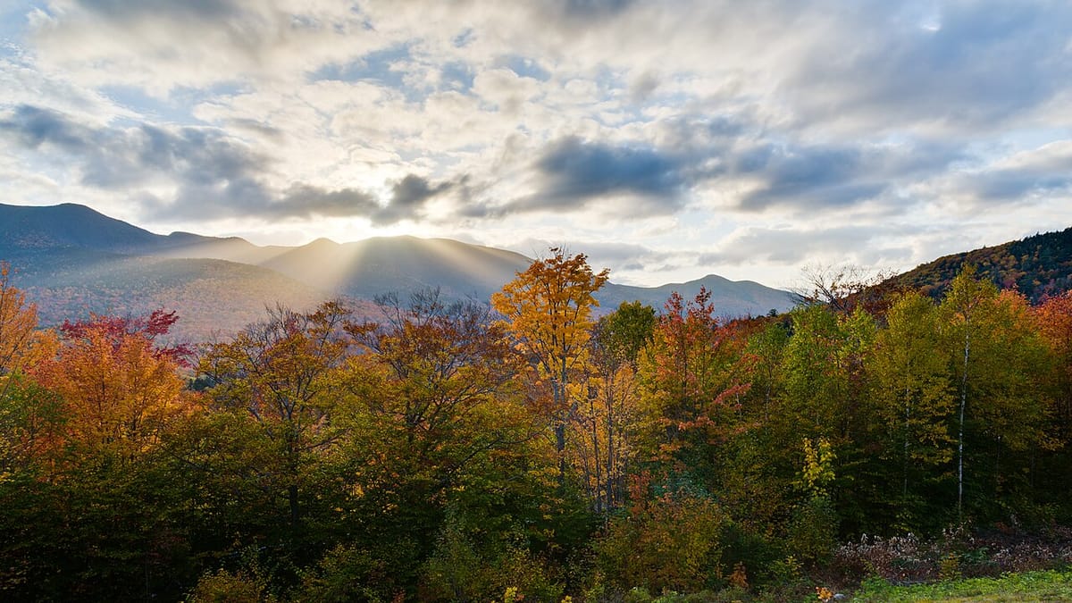 New Hampshire's White Mountains at peak color, sunlight breaking through cloud over the ridgeline